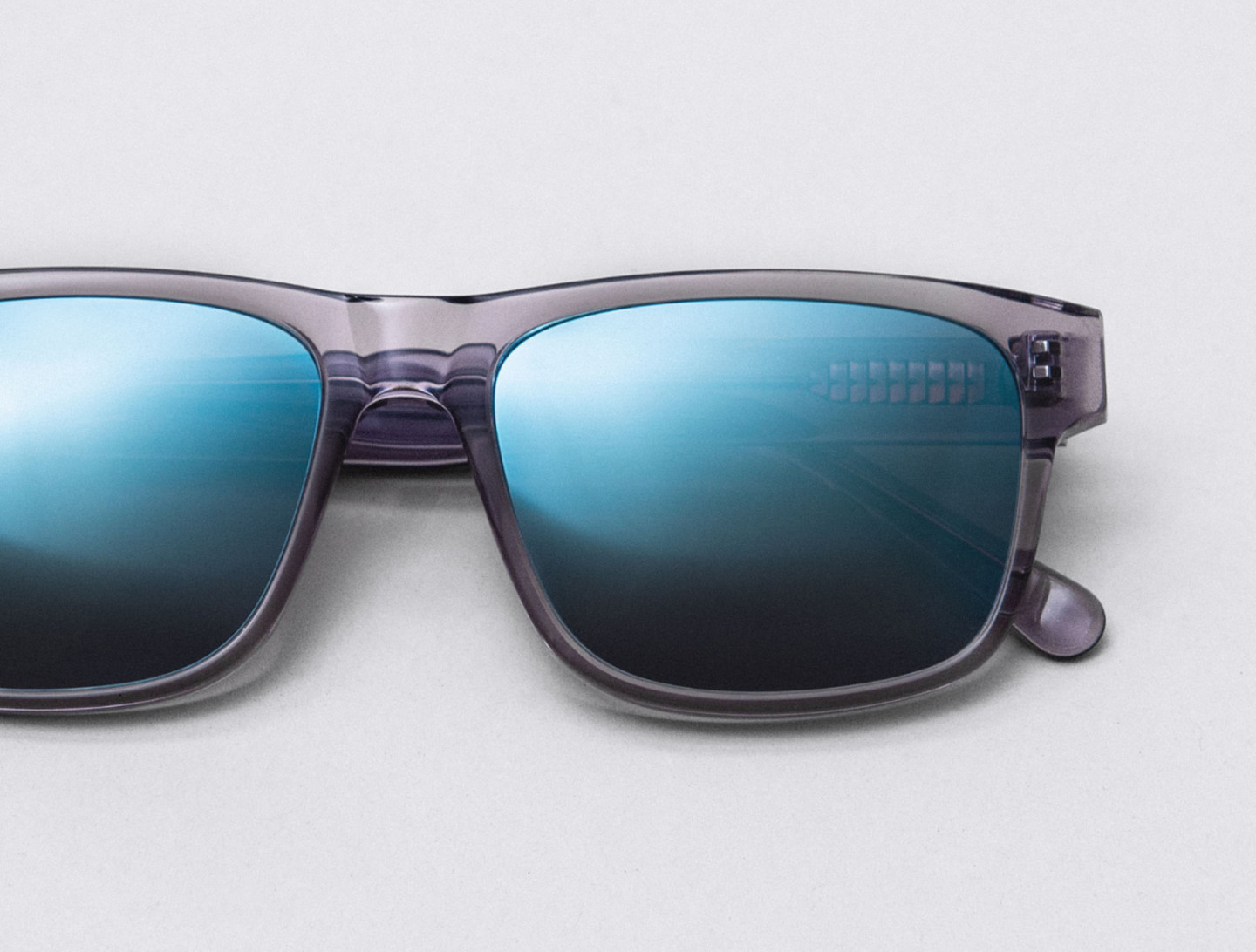 Nahaufnahme einer Sonnenbrille mit grau/transparentem Rahmen und blau verspiegelten Gläsern